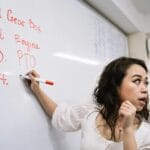 Dziennik lekcyjny kiedyś i dziś: od pióra i pieczęci do e-dziennika Nauczycielka zapisuje definicje techniczne na białej tablicy