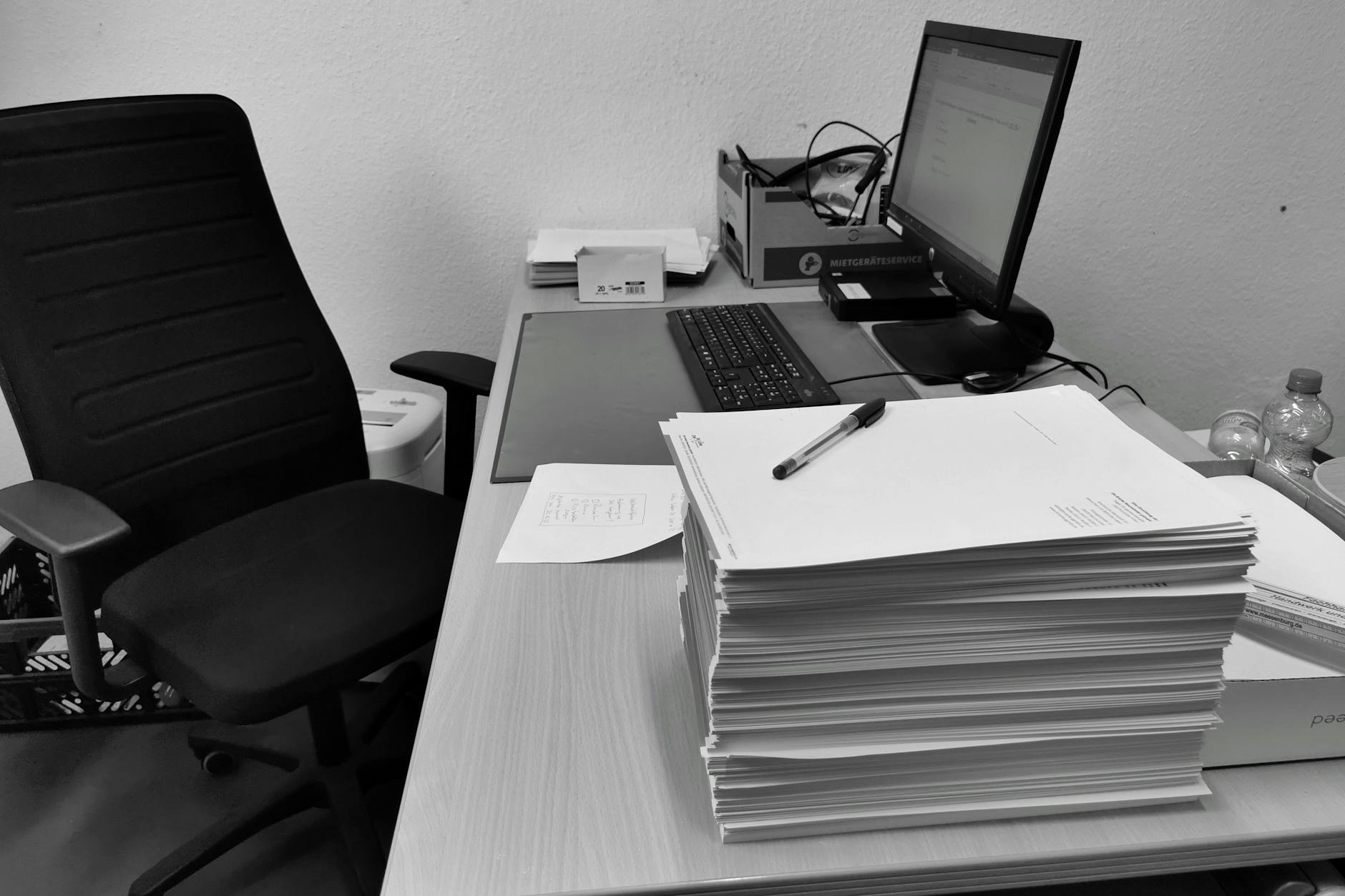 Czarno-białe biurko w dziekanacie z komputerem, krzesłem i stertą dokumentów