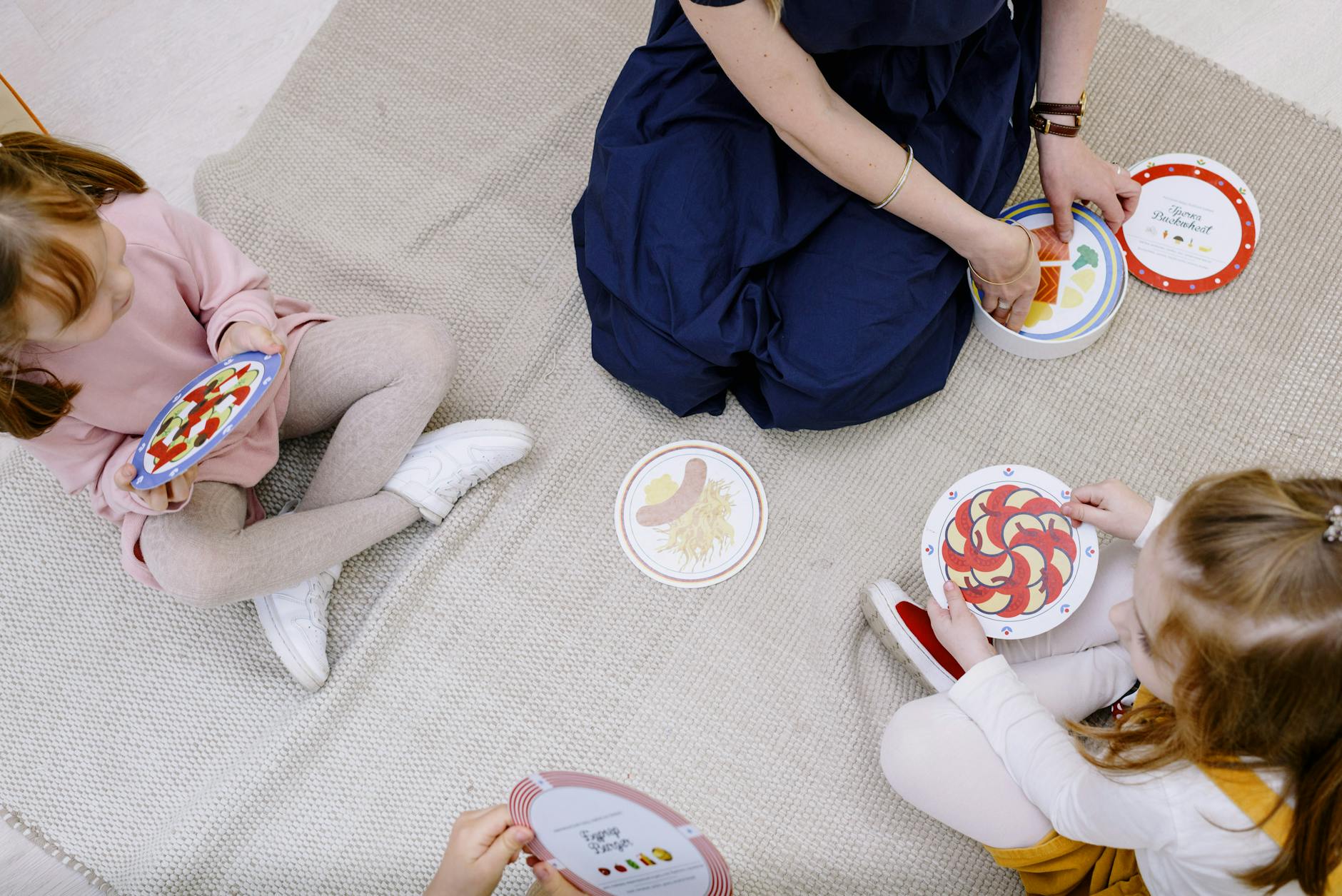 Nauczyciel gra w edukacyjną grę karcianą z trojgiem dzieci na kocu