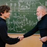Jak negocjować warunki zatrudnienia w szkole bez konfliktu i z korzyścią dla obu stron Profesor i student podają sobie ręce przed tablicą z wzorami matematycznymi